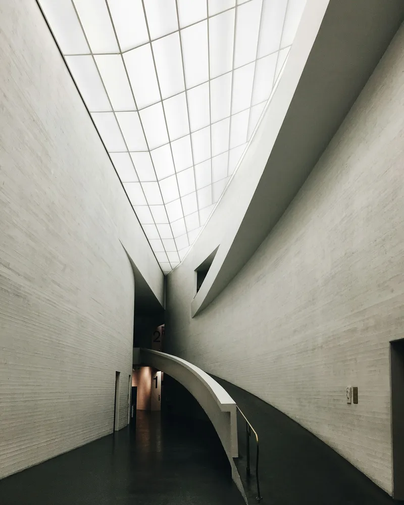 A tall gallery interior with a curved staircase, pale brick walls and a glazed roof.