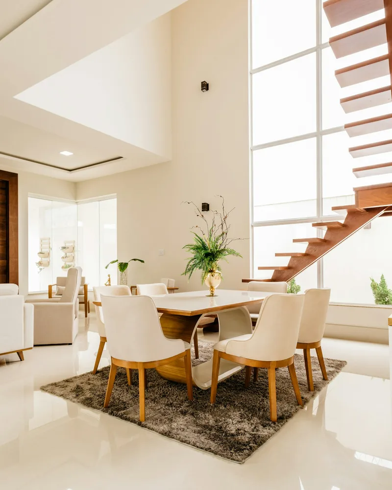 A bright double-height living and dining room with timber stairs and cream furniture.