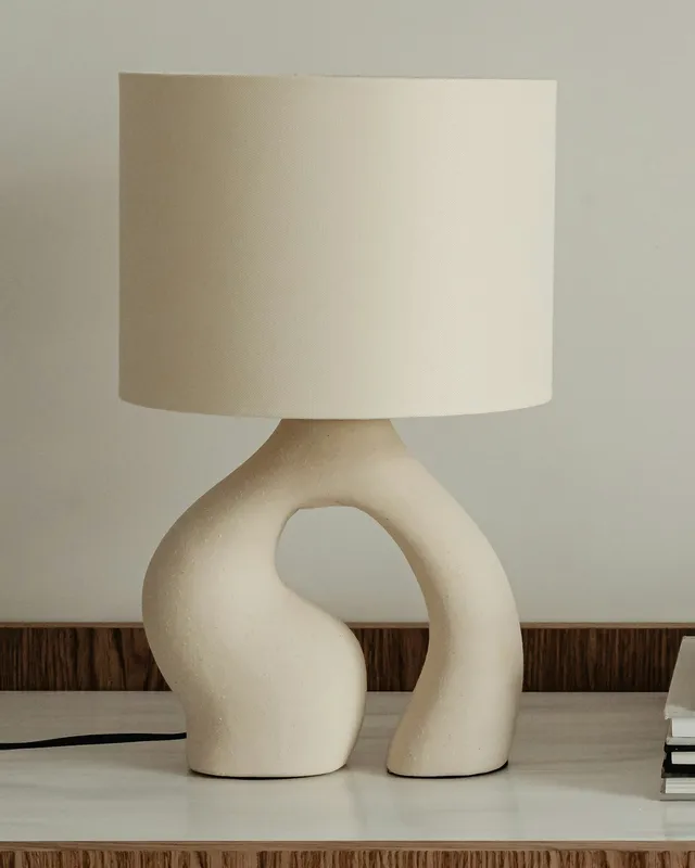 A cream table lamp with a curved sculptural base and a cylindrical shade.