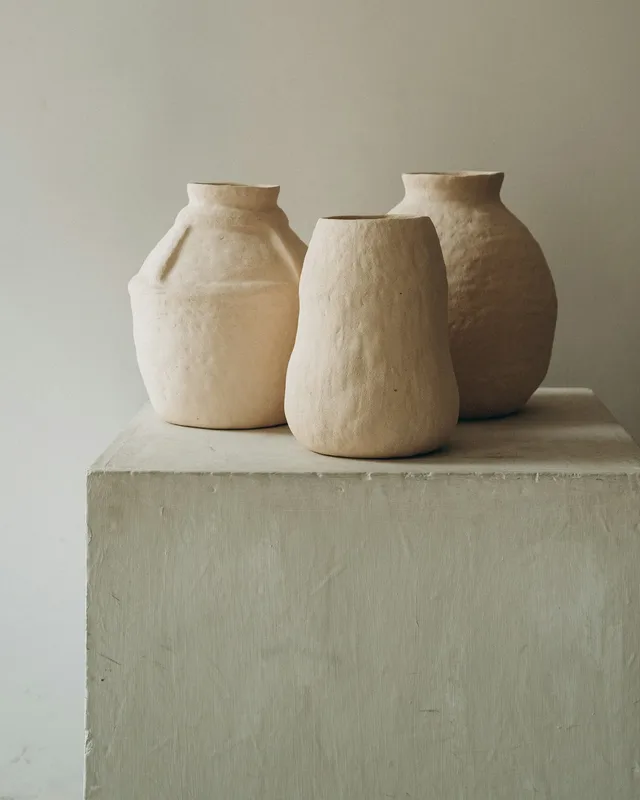 Three textured cream ceramic vases on a pale plinth.